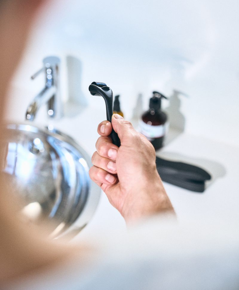 Mann hält einen Bartroller über dem Waschbecken – Bartpflege-Tool zur Förderung des Bartwuchses.