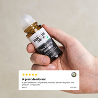 Hand holding a Brooklyn Soap Company Deo Roll-On bottle, with a visible customer review below praising the product’s reliable protection, pleasant scent, and skin compatibility.[INT][EU]