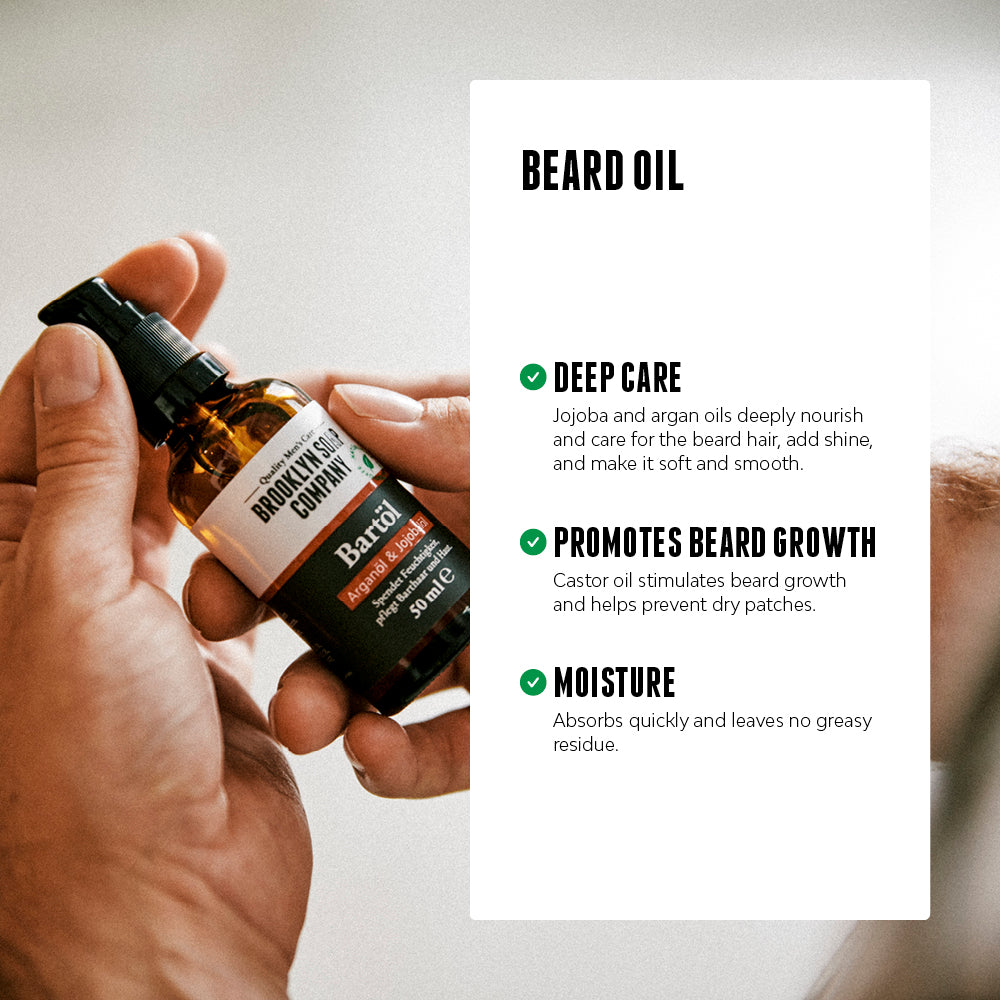A hand holding a Brooklyn Soap Company Beard Oil bottle with text listing benefits: deep nourishment from jojoba and argan oil, support for beard growth via castor oil, and quick absorption without residue.[INT][EU]